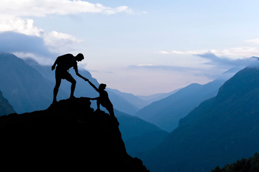 Image of one person helping another up a mountain
