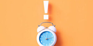 Exclamation point sitting over white alarm clock on orange background. Horizontal composition with copy space.